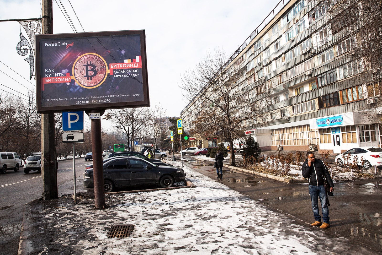 Man takes a phone call next to a Bitcoin billboard outside on a snowy day in Kazakhstan