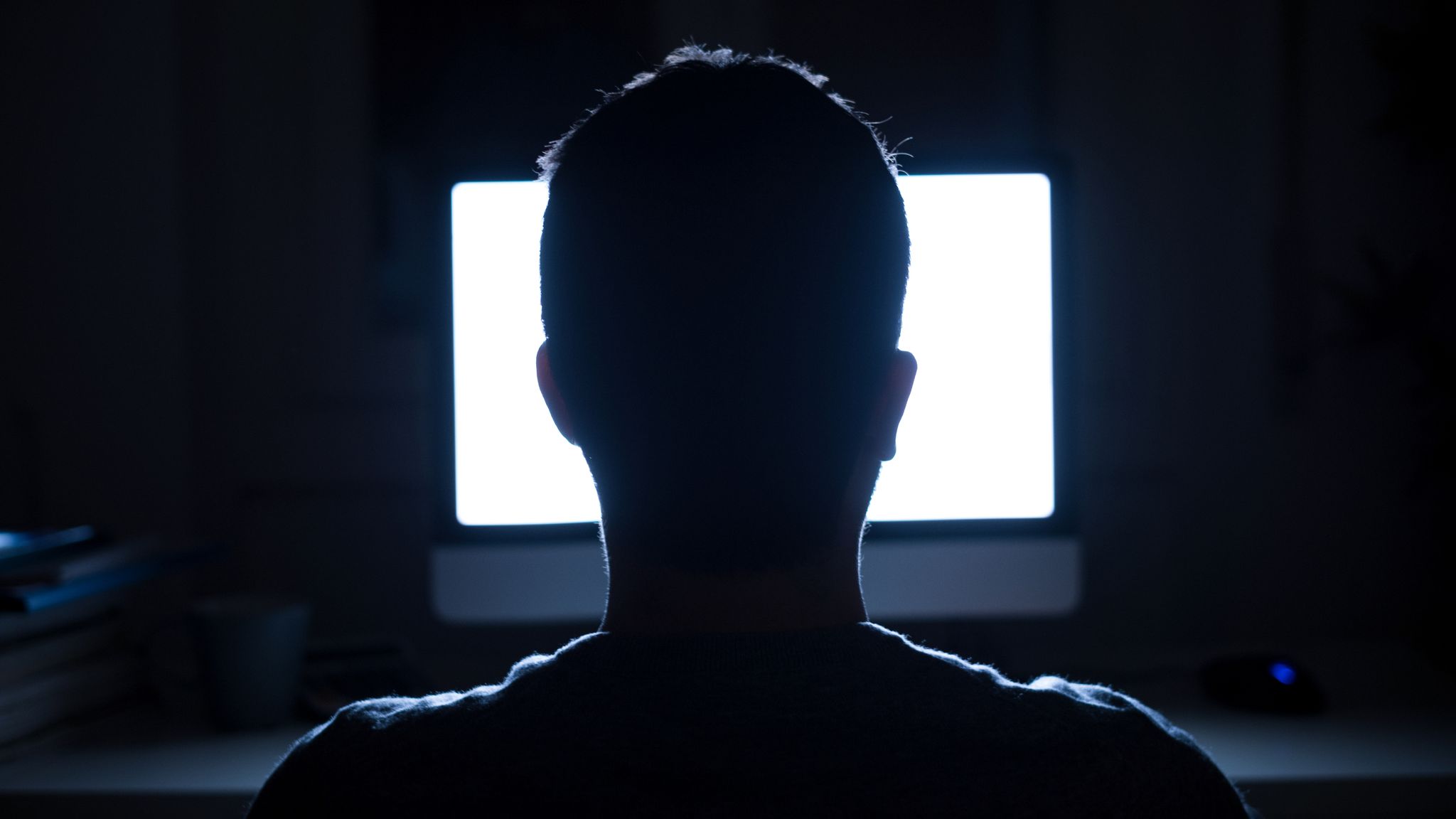Silhouette of man&#39;s head in front of computer monitor light at night
