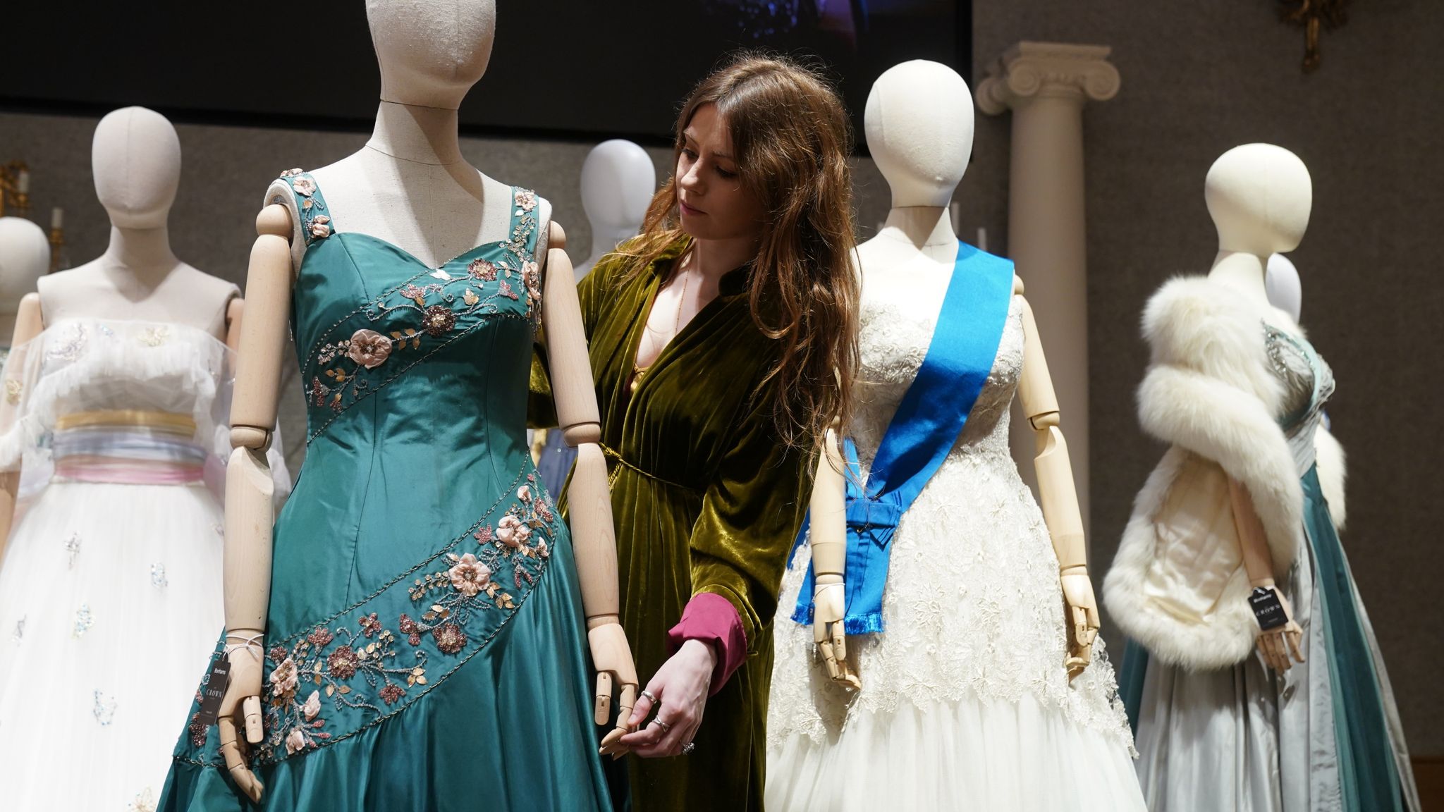 A gallery assistant adjusts a replica of a gown worn by Queen Elizabeth II, which is part of the collection of more than 450 costumes, sets and props from the Netflix series The Crown, on show at Bonhams in central London, ahead of being auctioned next month. Picture date: Tuesday January 9, 2024. 