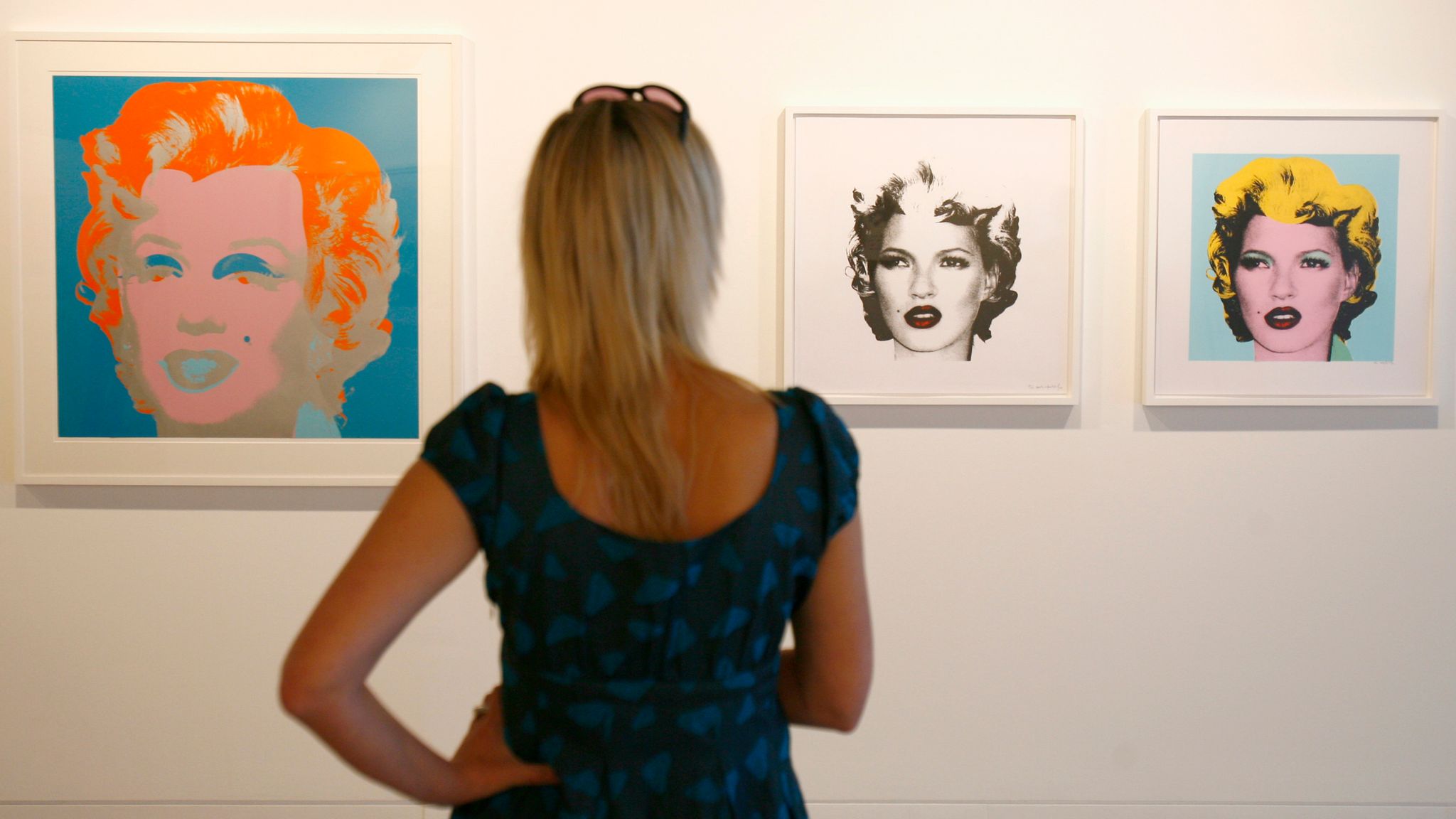 An woman looks at "Marilyn 29" (L) by artist Andy Warhol and "Kate Moss (Black)" and "Kate Moss (Yellow)" by Banksy, part of the exhibition Warhol vs Banksy at The Hospital in Covent Garden, London, August 9, 2007. It is the first joint exhibition of the two artists and runs until September 1, 2007. REUTERS/Luke MacGregor (BRITAIN) 