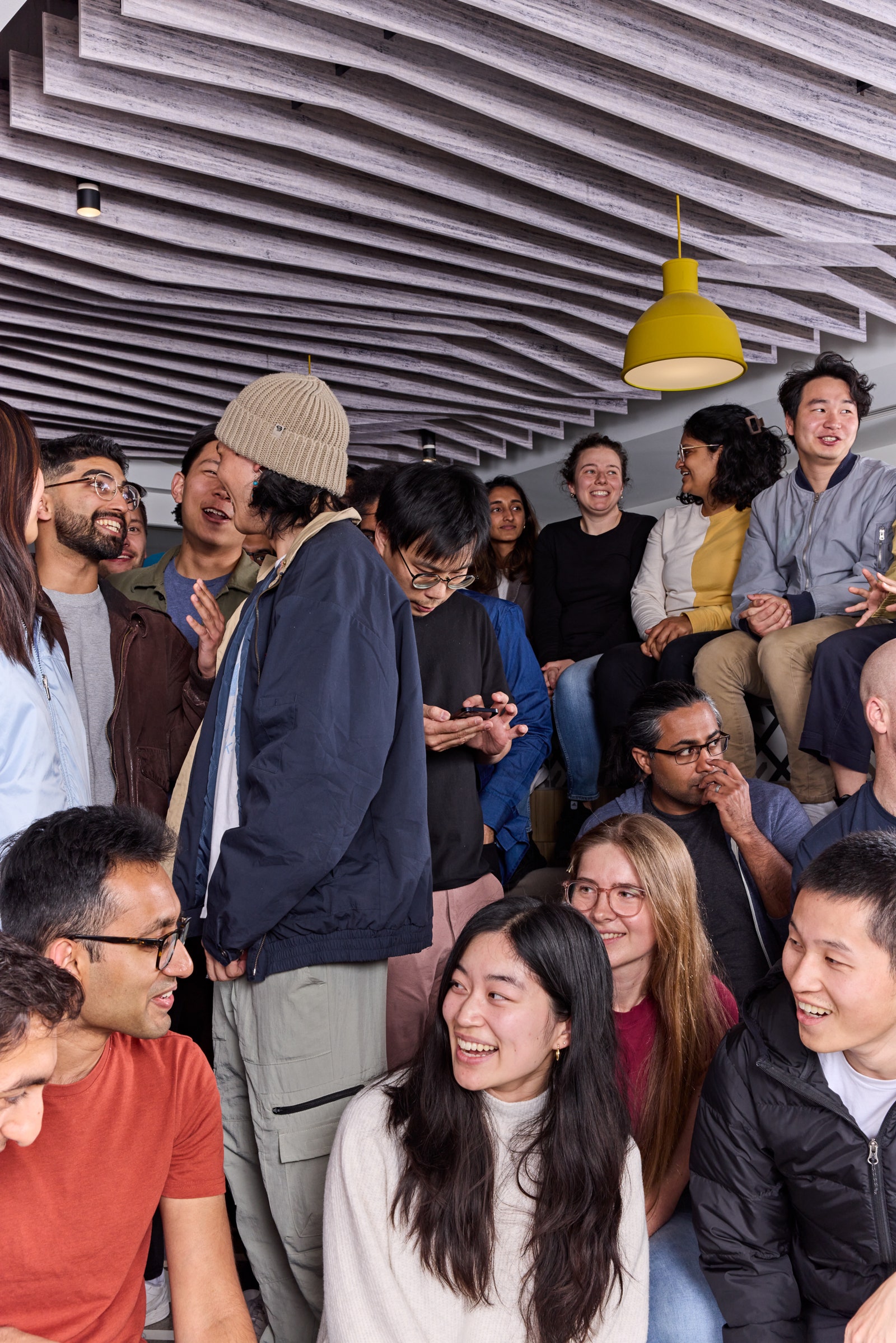 A crowded group of people talking smiling and checking their smartphones in an office space