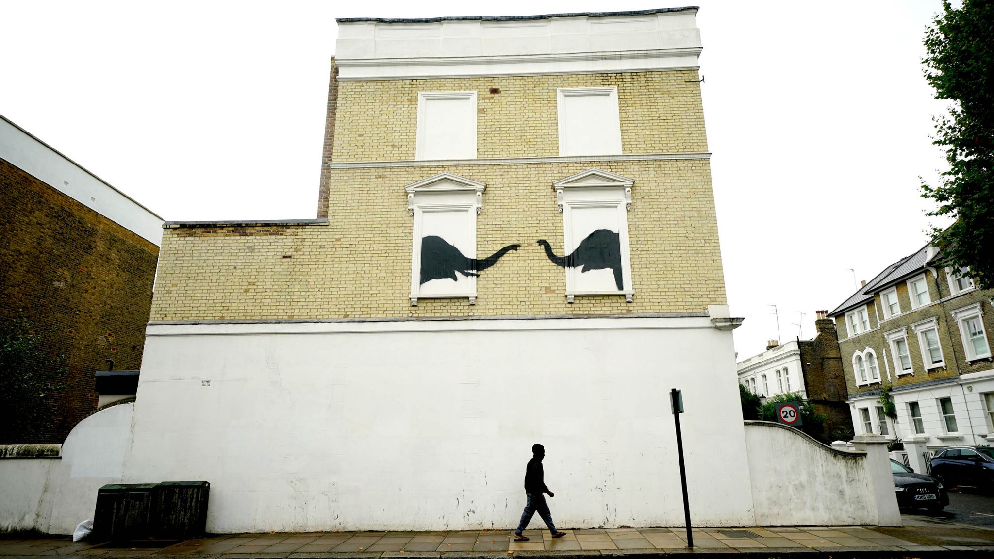 A man passes underneath a new artwork depicting two elephants poking their heads out of blocked out windows unveiled by Banksy on the side of a building at the junction of Edith Grove and Edith Terrace, in Chelsea. Pic:PA